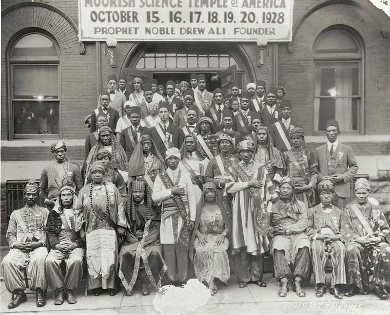 1928
Members of the Moorish Science Temple of America posing before meeting place during annual gathering, October 1928; Prophet Noble Drew Ali Founder [first row, standing, fifth from left.
Moorish Science Temple of America photograph collection. 
